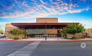 A modern convention center with a large glass facade and a cantilevered roof, under a dramatic cloudy sky.