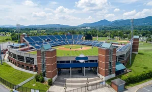 Aerial view of a baseball stadium with blue seats, a green field, and mountains in the background.