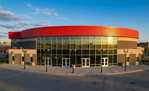 Modern circular building with red roof and large glass windows, reflecting the blue sky.