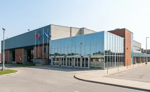 Modern building with glass facade and brick accents, featuring flags and a parking lot.