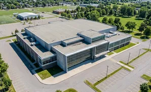 Aerial view of a modern building with large windows, surrounded by parking lots and green spaces.