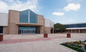 Exterior of a modern building with large glass windows and stone accents, a courtyard with planters and a sculpture.