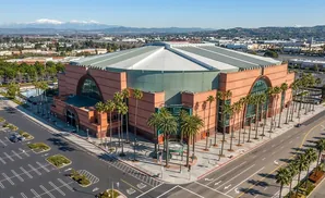 Aerial view of the Anaheim Convention Center with palm trees and distant snow-capped mountains.