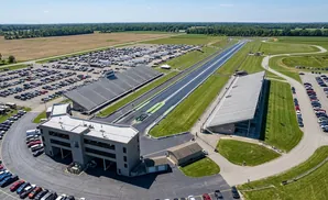 Aerial view of a drag strip with grandstands and large parking lots filled with cars.