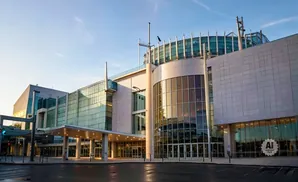 Modern convention center with a curved glass facade and stone accents, under a clear blue sky.