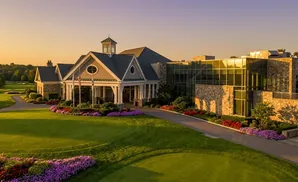 Golf clubhouse with stone and glass architecture, surrounded by lush green lawns and colorful flower beds.