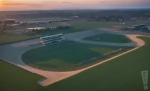 Aerial view of a horse racing track at sunset, with grandstands and surrounding fields.