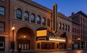 An ornate brick theater facade with a marquee lights up at dusk.