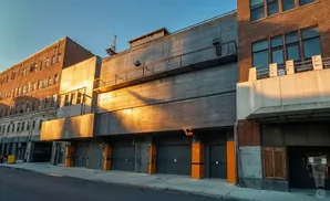 Sunlight illuminates the side of a brick and concrete industrial building with multiple garage doors.