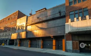 Modern building with brick and concrete facade, garages, and windows, bathed in golden hour light.