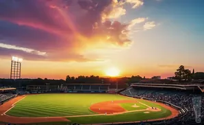 A baseball stadium at sunset with a vibrant sky and illuminated field.