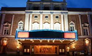 An ornate brick theater glows at dusk, featuring a marquee with red panels and illuminated windows.