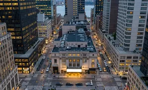 Aerial view of a city street with tall buildings, cars, and pedestrians at dusk.