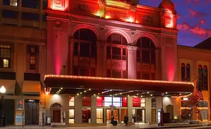 Exterior of a historic theater lit up in red at dusk, with a marquee and arched windows.