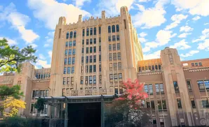Art Deco building with ornate stone facade and tall vertical windows, under a blue sky with white clouds.