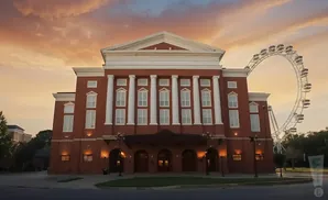 A neoclassical brick building with columns and windows under a sunset sky, with a Ferris wheel in the background.