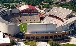 Aerial view of a large stadium with a red-roofed building and tiered seating overlooking a football field.
