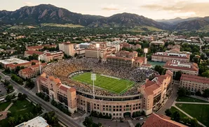 Aerial view of a football stadium filled with fans, surrounded by university buildings and mountains.