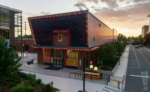 Modern building with red and gold lights on the roof, at dusk with a street and cars.