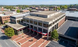Aerial view of a brick and concrete building with a parking garage next to it under a clear sky.