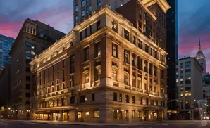 Ornate, well-lit building on a city street at dusk, with a pink and purple sky.