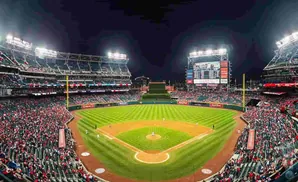 A baseball stadium at night, with bright lights illuminating the field and a packed crowd in the stands.