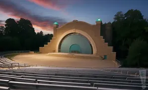 Outdoor amphitheater with tiered seating and a large arched stage at dusk with a colorful sky.