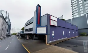 A purple cinema building with a vintage marquee and marquees above the entrance, on a cloudy day.