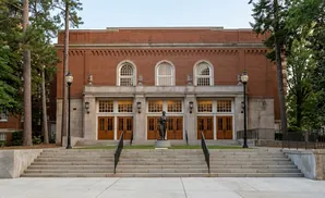 A brick building with large windows and doors, a statue, and a wide set of stairs.