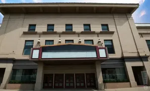 Front facade of a tan brick theater building with a marquee and multiple doors.
