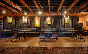 Interior of a restaurant with black booths, wooden tables, and framed art on a dark curtained wall.