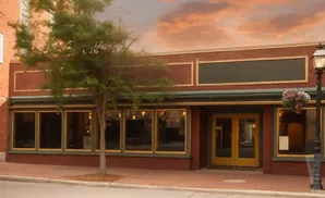 Exterior of a brick building with large windows, double yellow doors, and a street lamp with flowers.