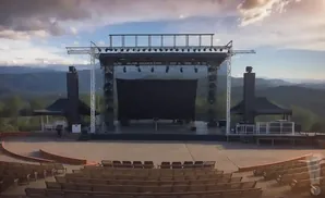 Outdoor amphitheater stage with seating in front and mountains in the background.