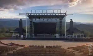 Outdoor amphitheater stage with tiered seating and a scenic mountain backdrop.