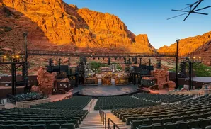Outdoor amphitheater with a stage set against red rock cliffs at sunset.