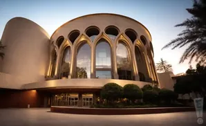 A modern building with a curved facade, large arched windows, and palm trees, bathed in soft evening light.