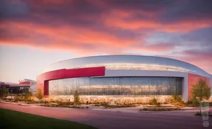 Modern stadium with glass facade and red accents against a dramatic sunset sky.
