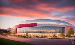 Modern stadium with large glass windows and red accents against a vibrant sunset sky.