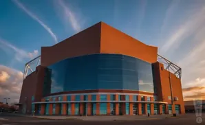 Large modern building with a curved glass facade and orange brick exterior under a blue sky with wispy clouds.