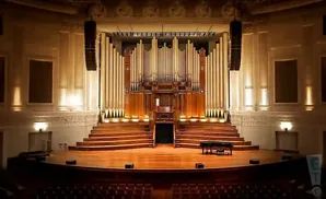 Grand pipe organ on a stage with a grand piano and tiered seating.