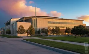 Modern building with large windows surrounded by green lawn and trees at sunset.