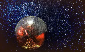 A disco ball reflects red and gold light against a dark blue, sparkling background.