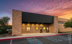 Modern building with stone facade and black metal roof at sunset.