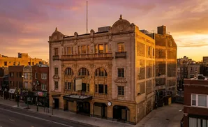 Ornate vintage building at sunset with glowing orange sky and purple clouds.