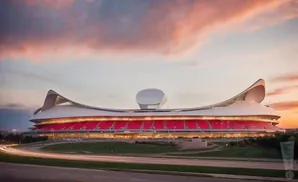 A modern stadium with red seats and a curved white roof at sunset.