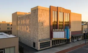 An exterior view of the Admiral Theatre, with warm sunlight highlighting its textured facade and marquee.
