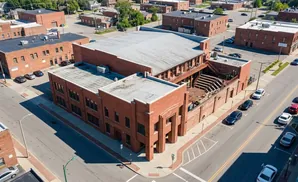 Aerial view of a red brick building with a large, flat roof, featuring an outdoor amphitheater and surrounding parking lot.