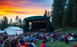 An outdoor concert at sunset with a crowd seated on grass in front of a stage.