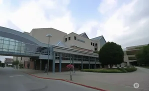 Modern building with a skywalk and a large green tree in front.