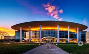 Modern building with a circular roof, glass facade, and dramatic sunset sky.